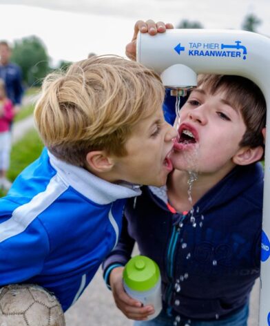 Kinderen drinken van een drinkwatertappunt van Waterbedrijf Groningen